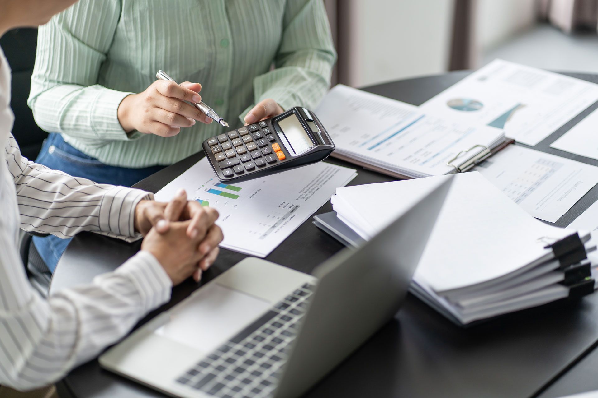 People reviewing financial documents with a calculator, laptop, and papers on a table.