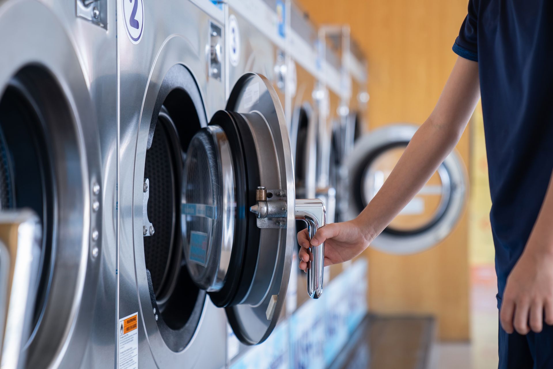 Person opening a washing machine door in a laundromat.