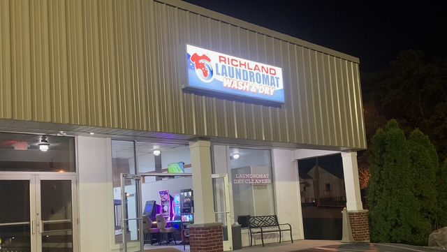 Woman operating a washing machine in a laundromat, pointing at the control panel.