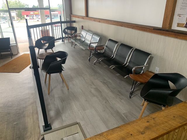 Waiting area with chairs and a metal bench. Gray flooring, wooden accents, and a railing.
