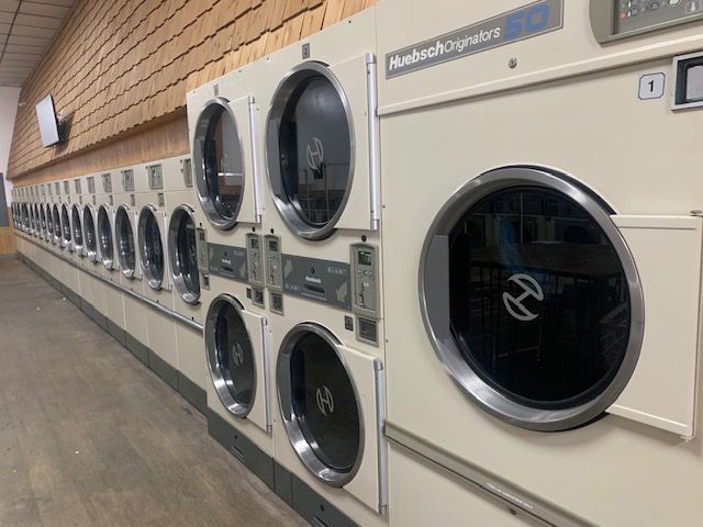 Row of commercial washing machines in a laundromat, cream-colored with large, circular doors.