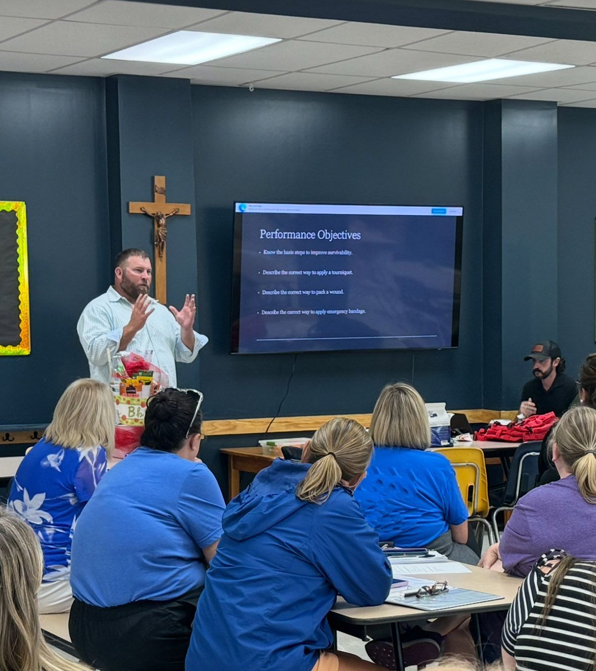 A man presents in a classroom to a group of teachers. He's standing near a screen with text.