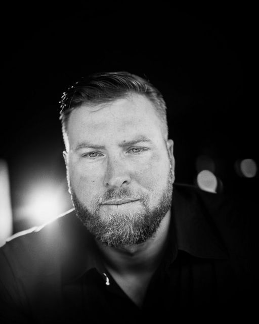 A man with a beard is looking at the camera in a black and white photo.