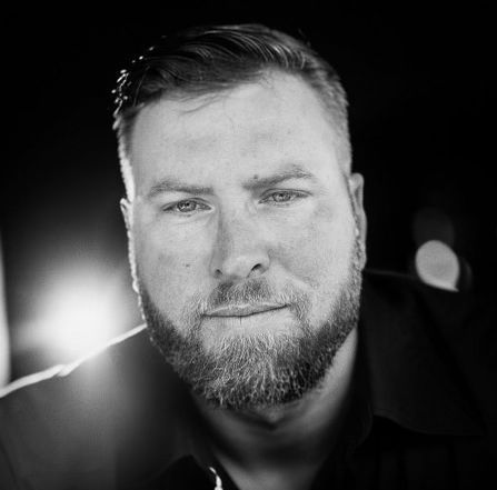 A man with a beard is looking at the camera in a black and white photo.