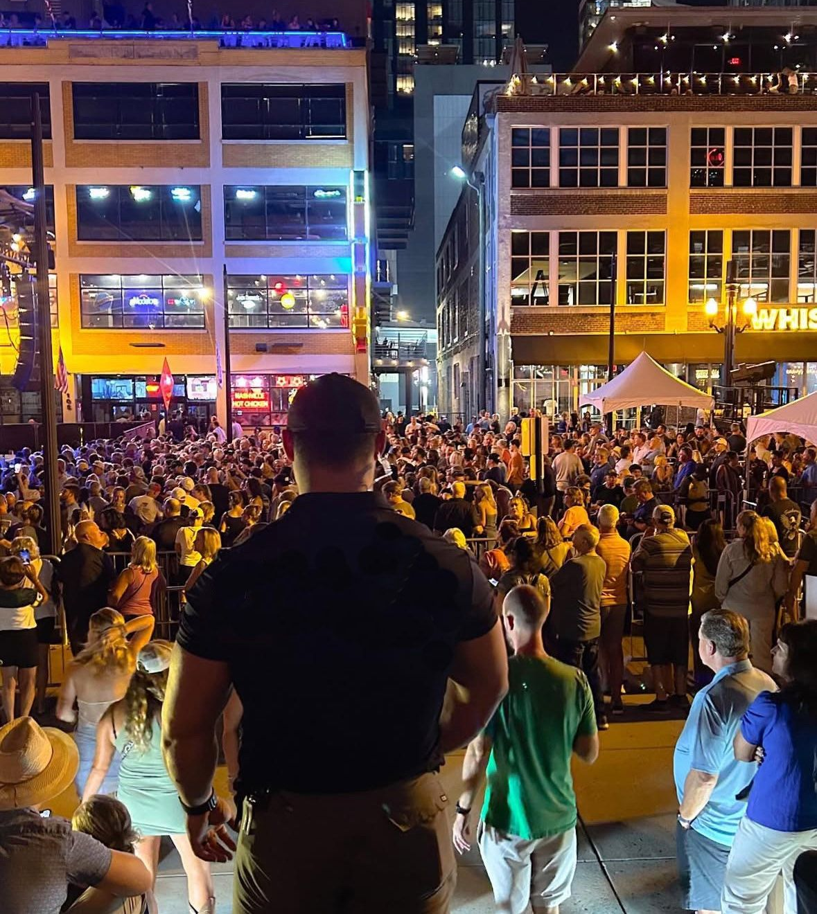 Man looking at large crowd in a brightly lit city street at night. Buildings and businesses surround.
