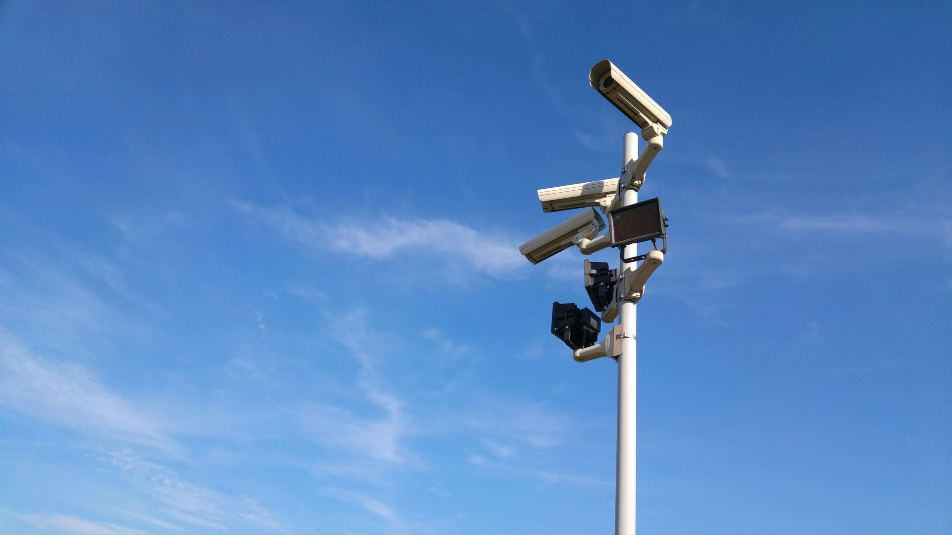 A bunch of security cameras on a pole against a blue sky
