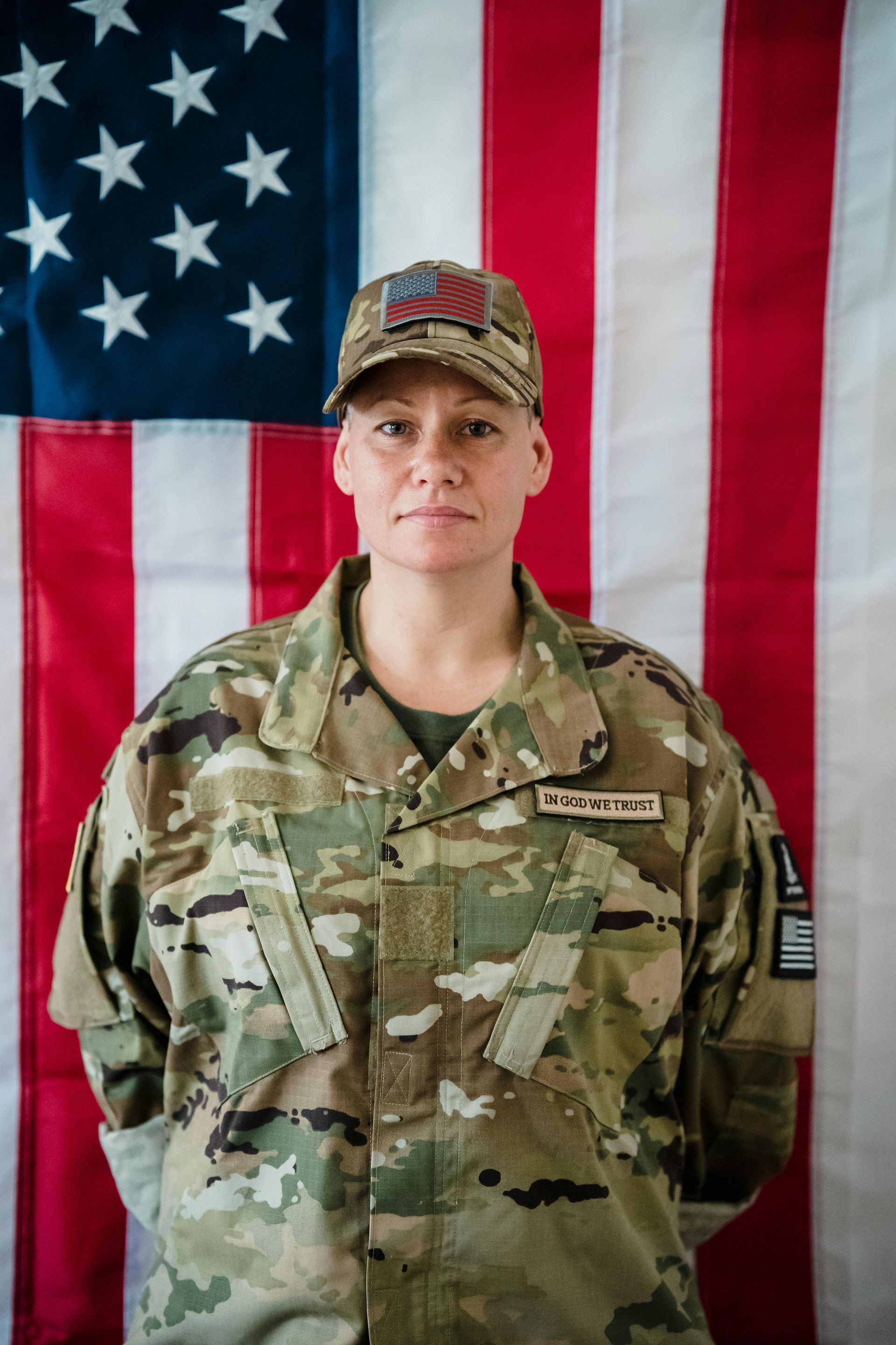 A woman in a military uniform stands in front of an american flag