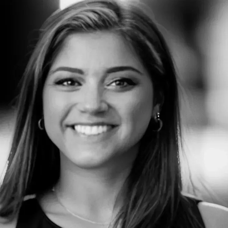 Smiling woman with dark hair, wearing a dark top, looking directly at the camera. Black and white.