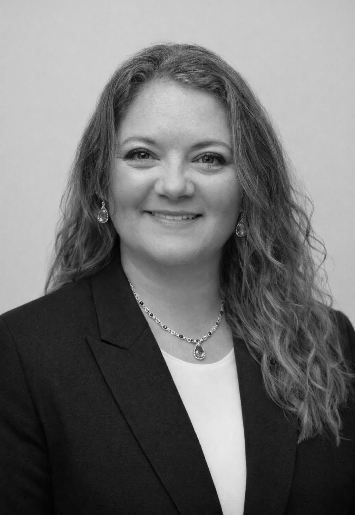 Woman in a blazer and necklace smiling.