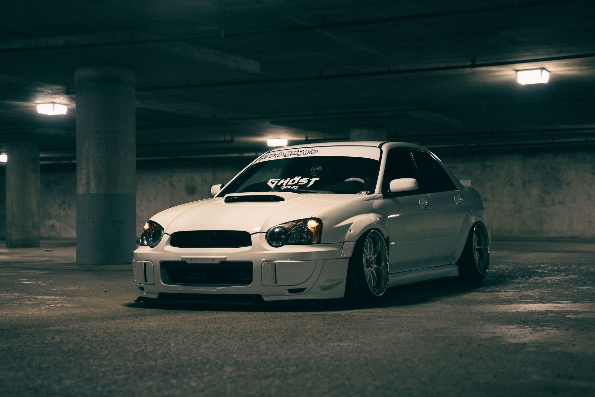 Low-Profile Vehicles Need Specialized Towing. White sports car parked in a dim underground garage, front three-quarter view.