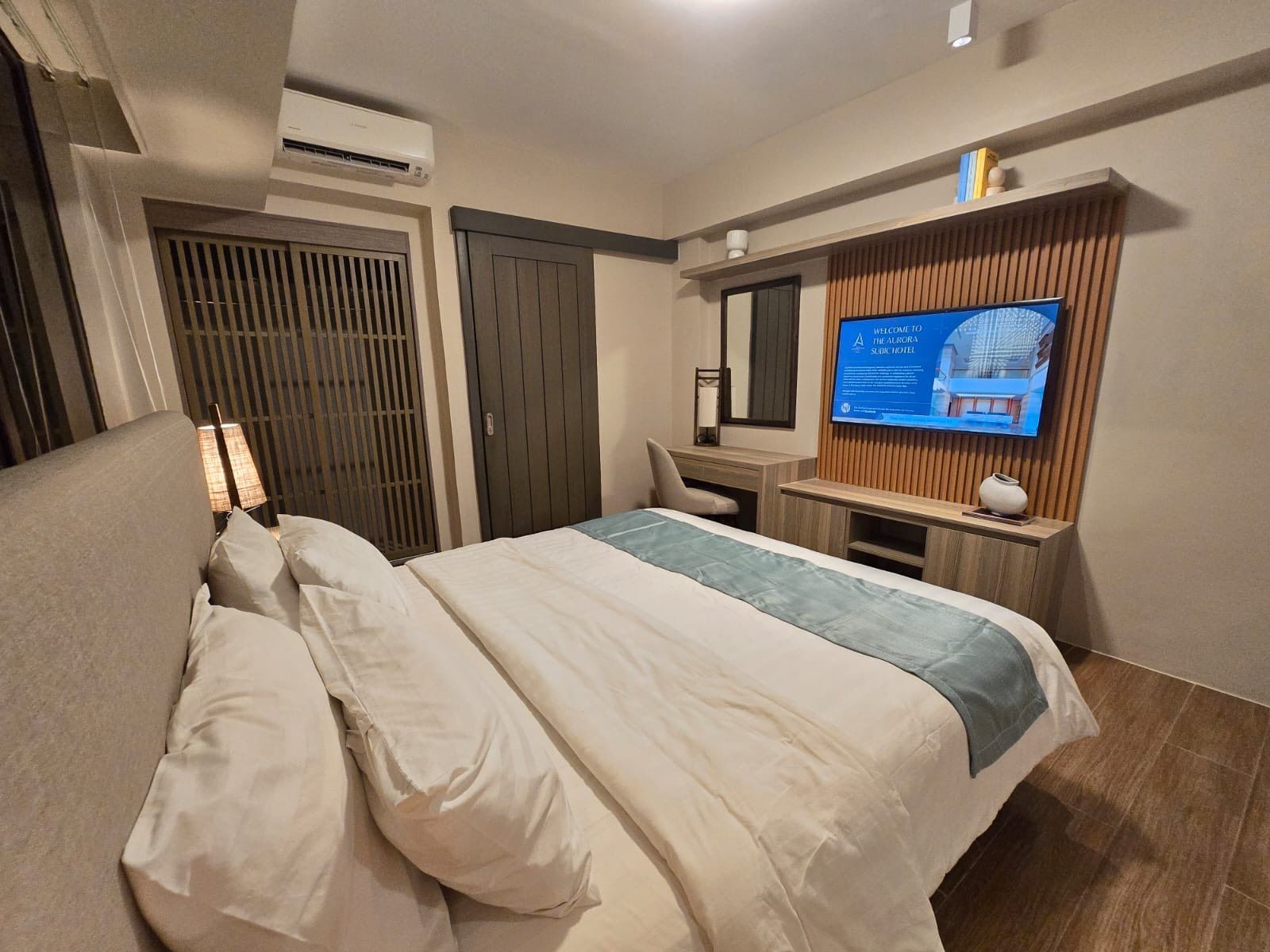Cozy hotel bedroom with unmade bed, wall-mounted TV, and balcony doors at night