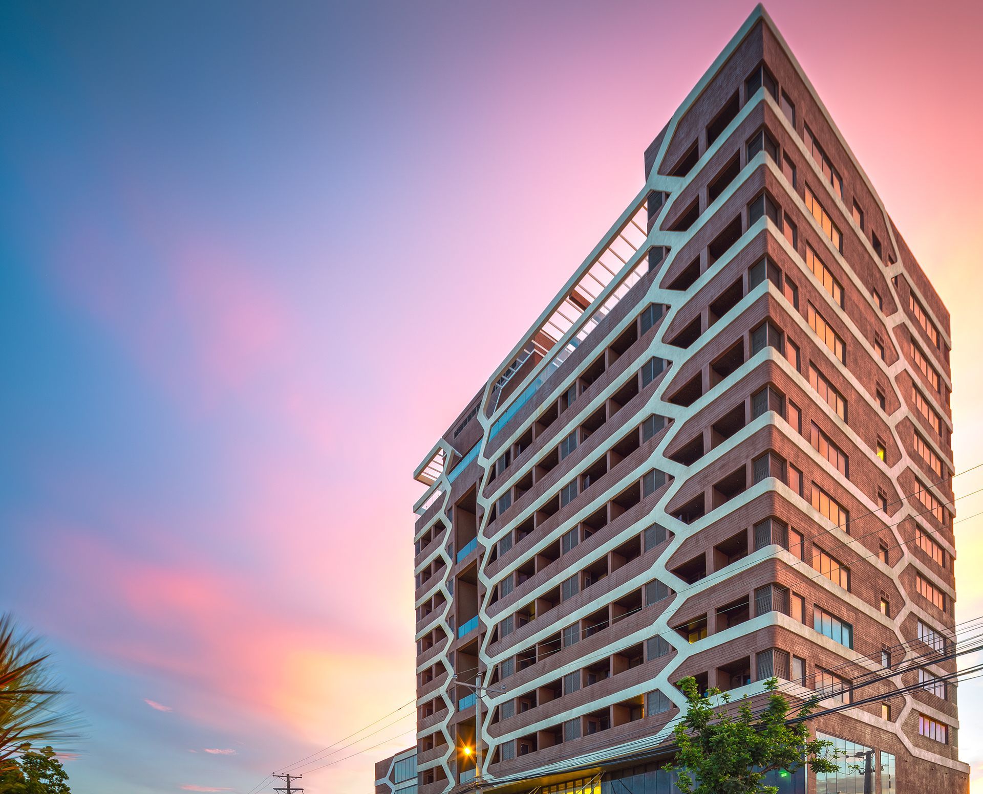 Modern high-rise building with brown and white facade against a colorful sunset sky.