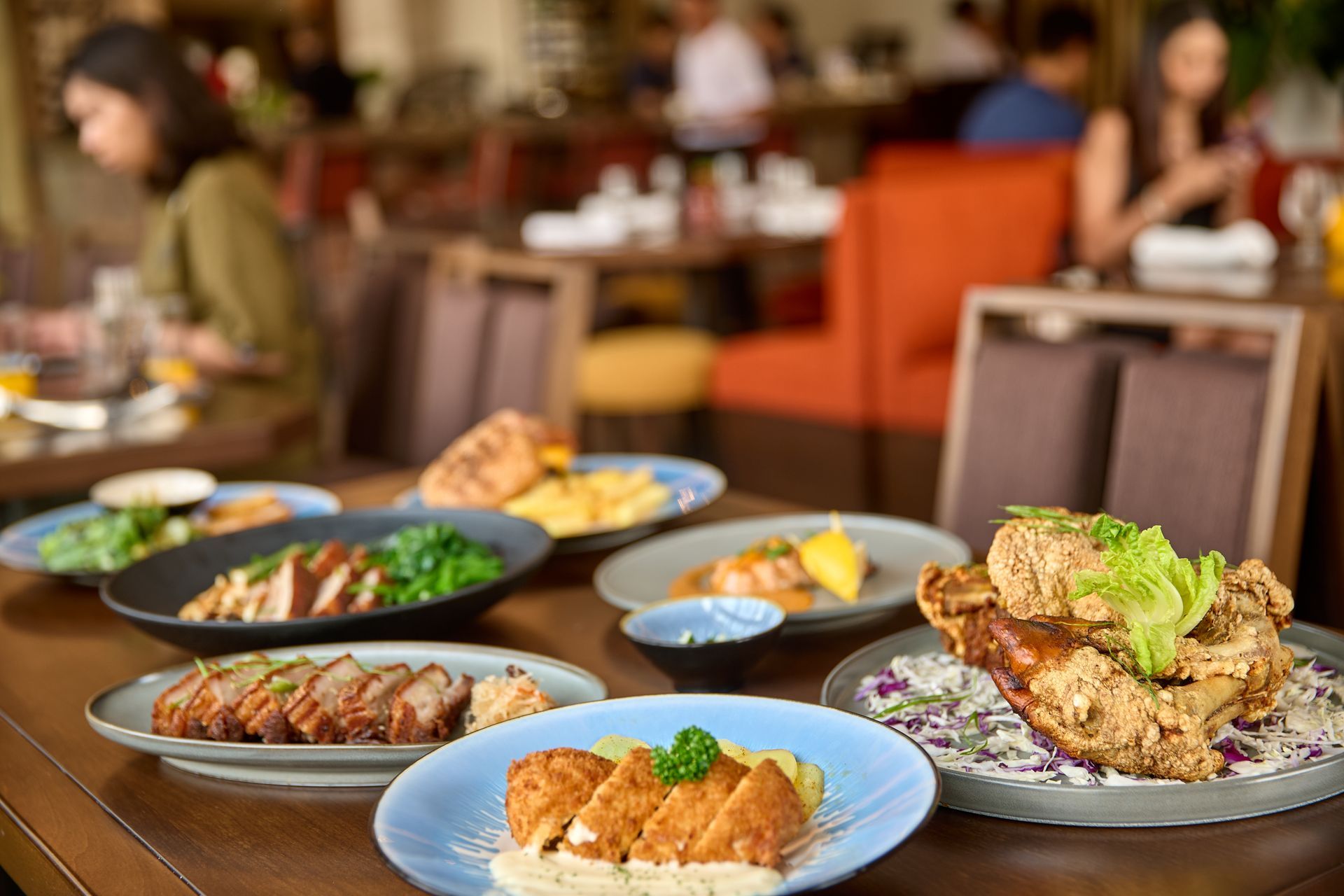 Table of food in a restaurant; roasted meats, fried chicken, salads, people dining.