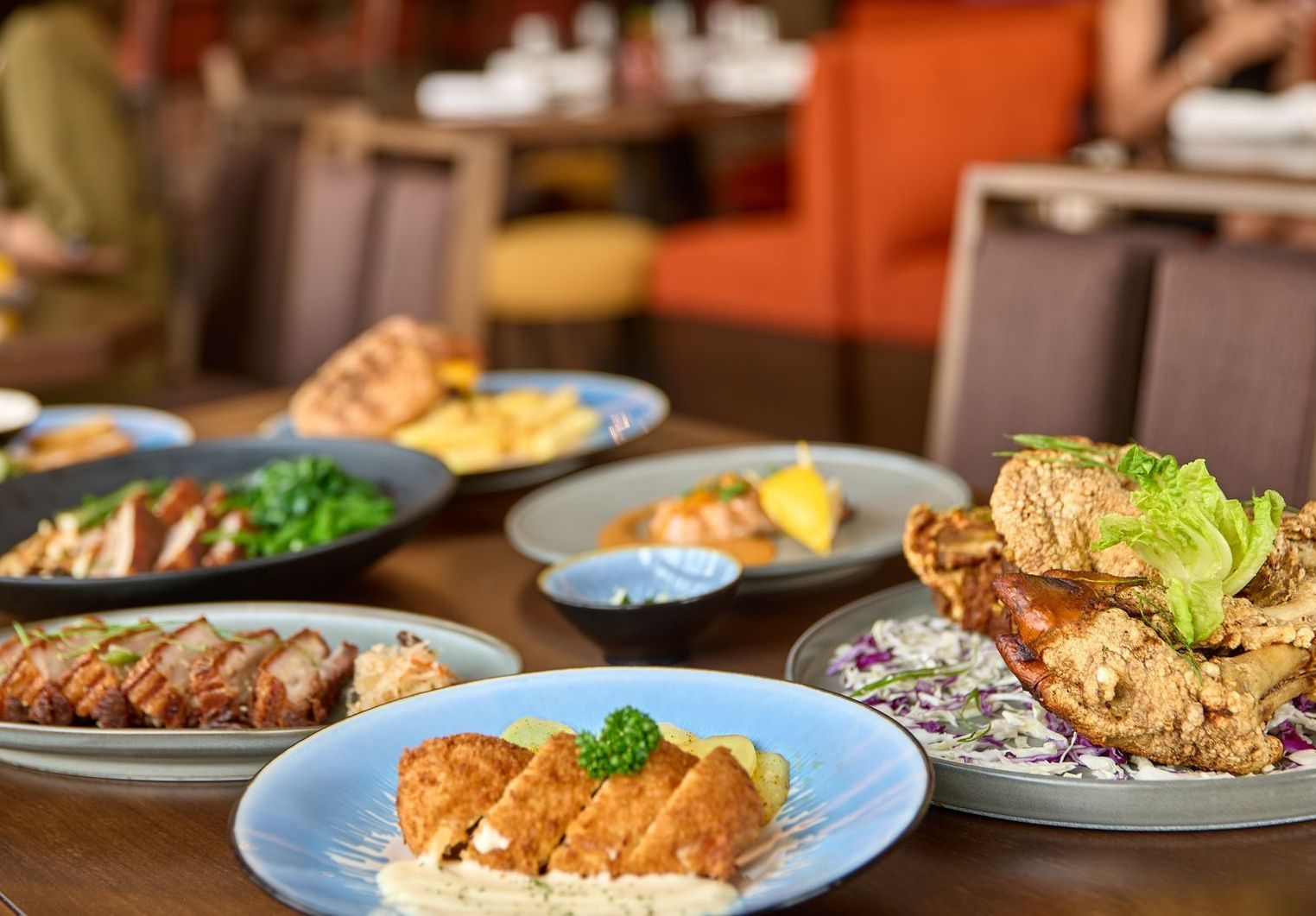 A variety of gourmet dishes, including fried chicken and sliced meat, are artfully arranged on a restaurant table.