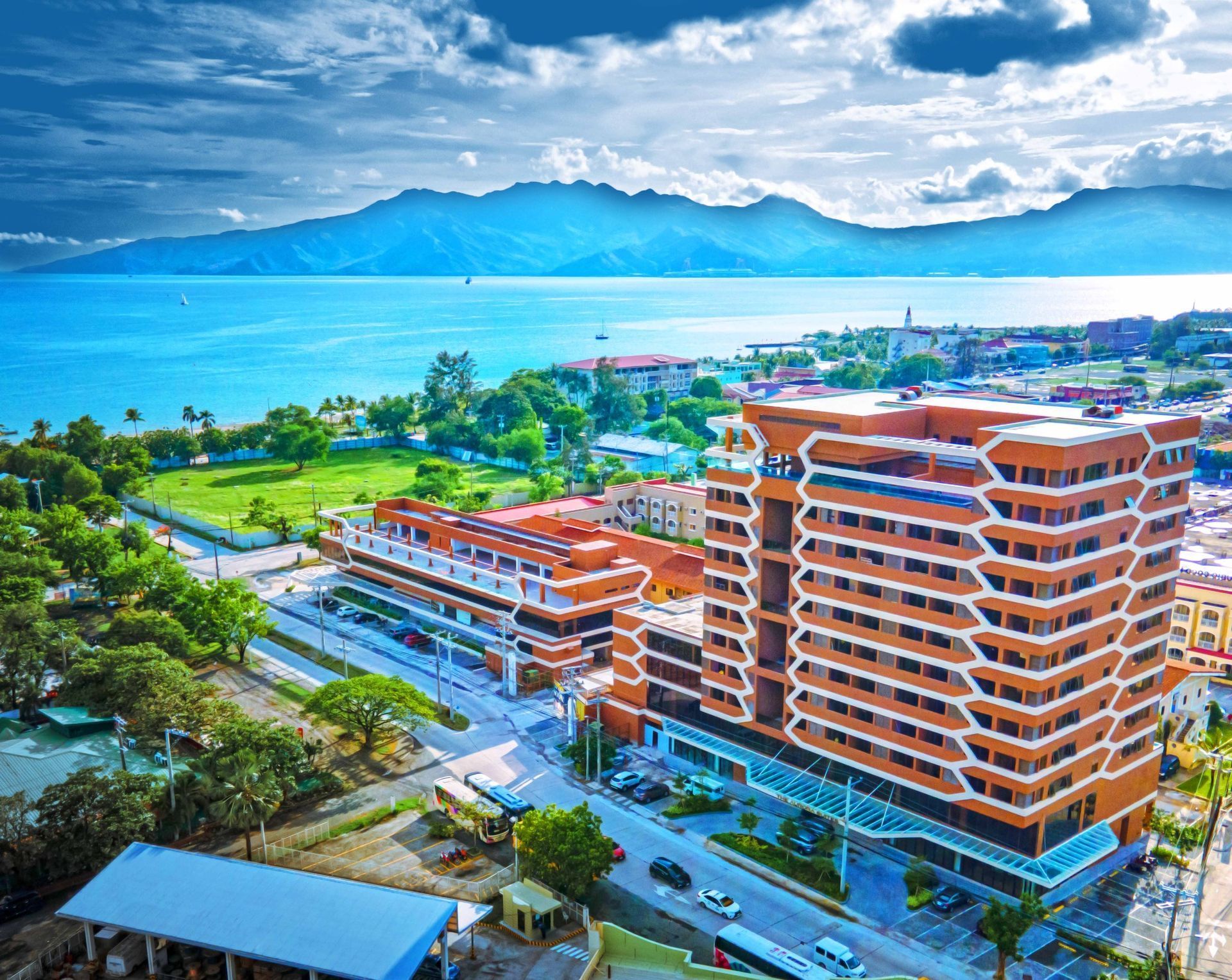 Coastal resort buildings with palm trees, road, and blue ocean with mountains in the background