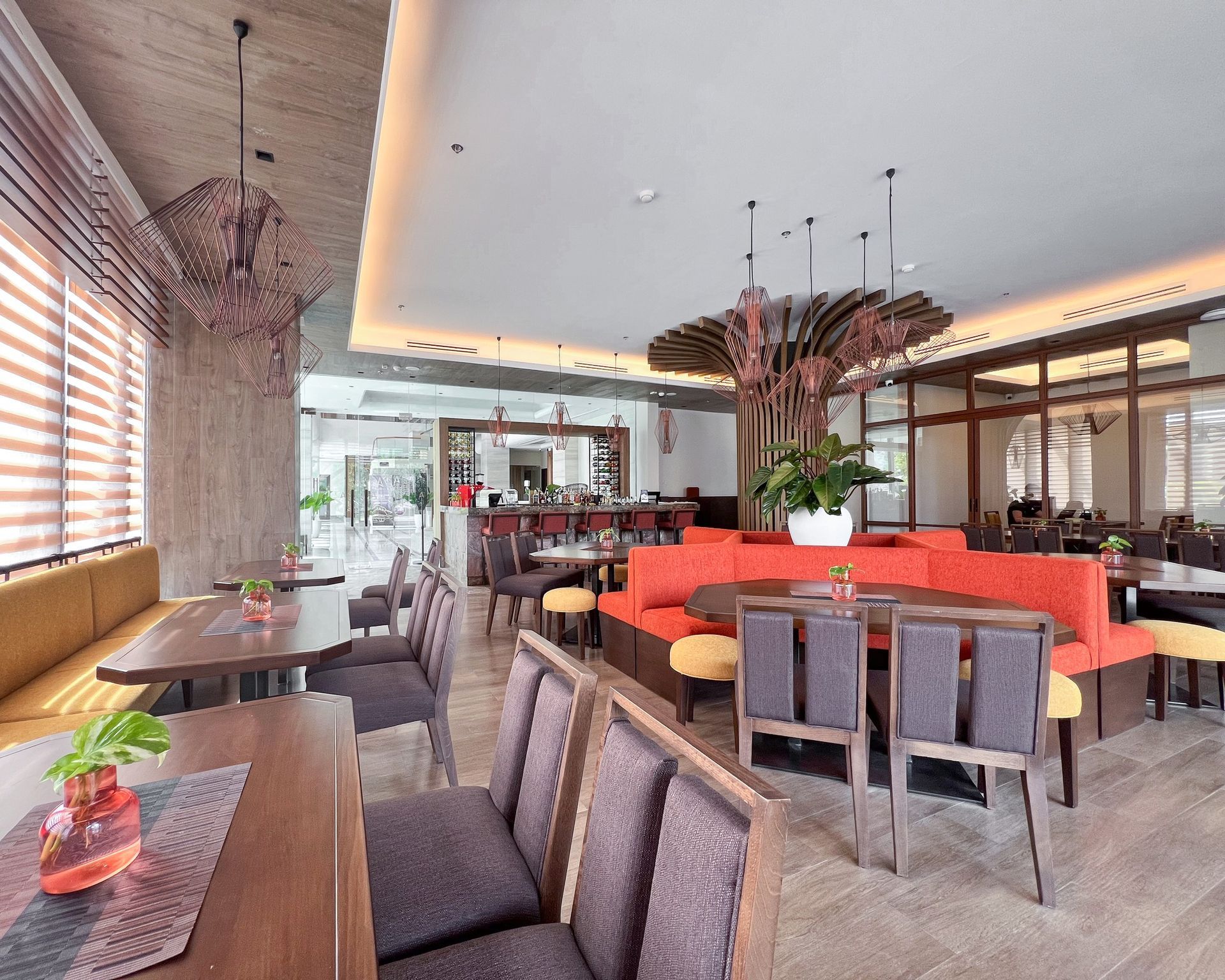 Modern restaurant interior with orange booths, dark chairs, pendant lights, and potted plants