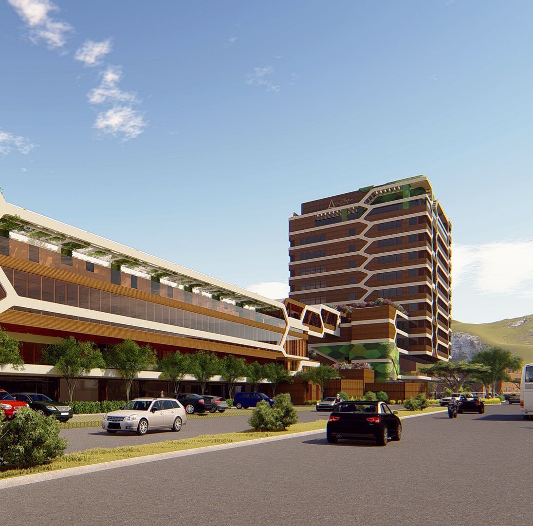 Modern building complex with a tall, brown honeycomb-patterned tower and a long, low-rise section with cars on a street.