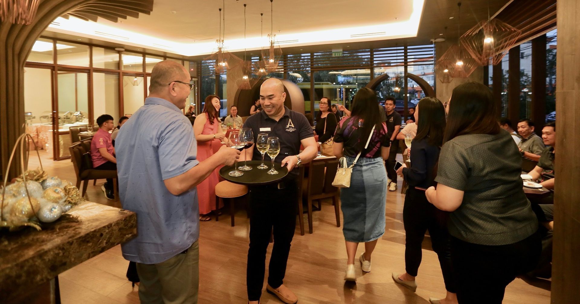 A group of people are standing in a room with a man holding a tray of wine glasses.