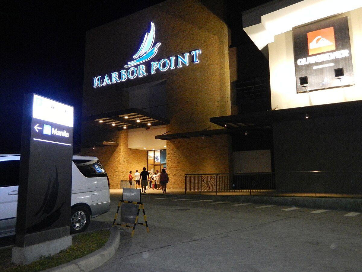 Harbor Point entrance at night with illuminated sign. A white car and people walking towards the entrance.