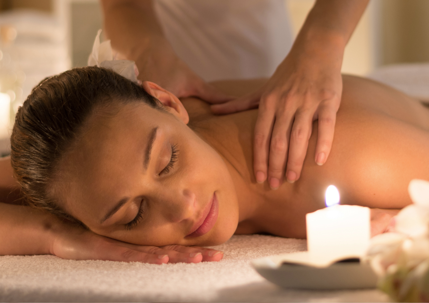 A woman is getting a massage at a spa with candles in the background.