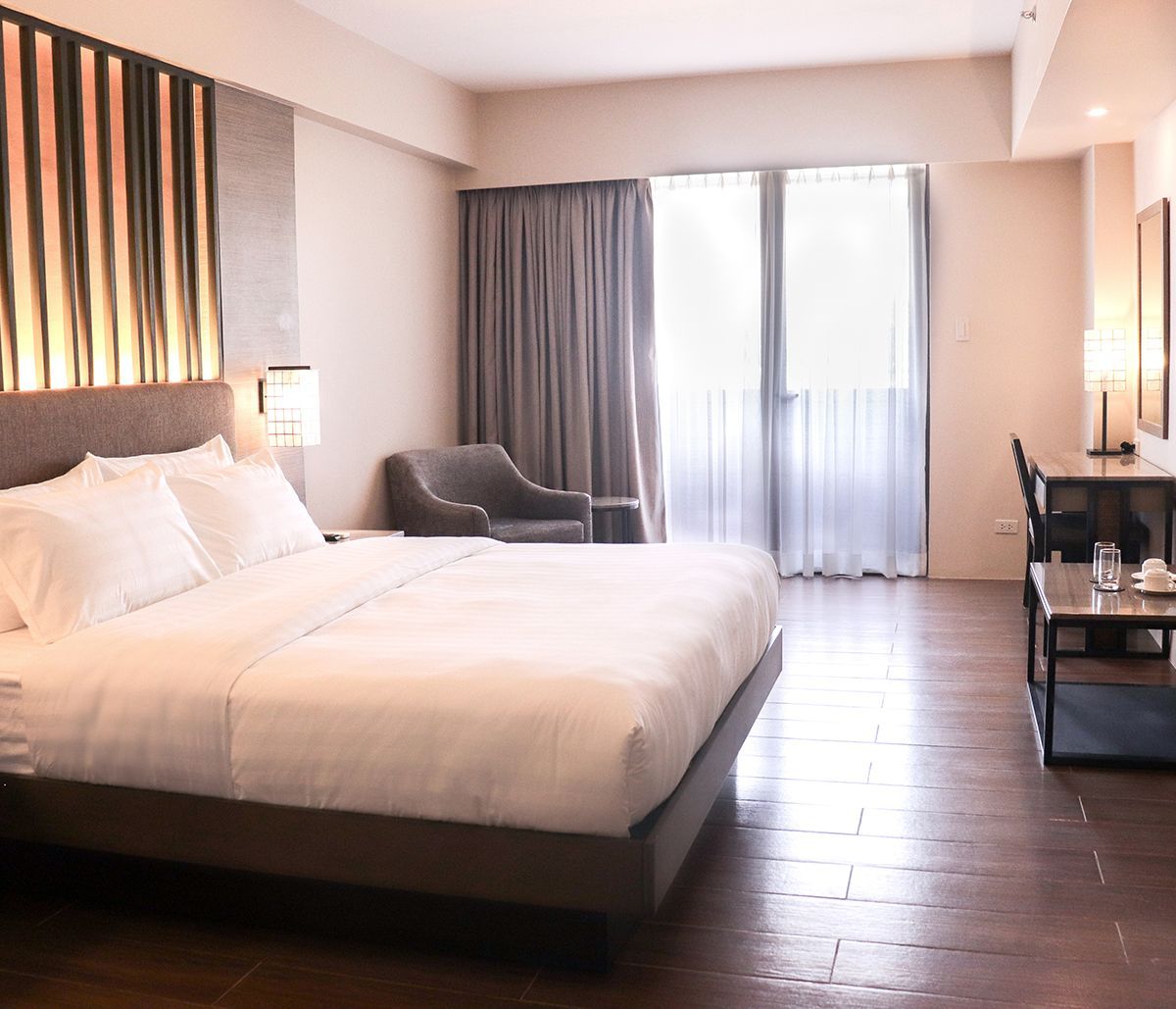 Hotel room with a large bed, armchair, desk, and balcony doors.