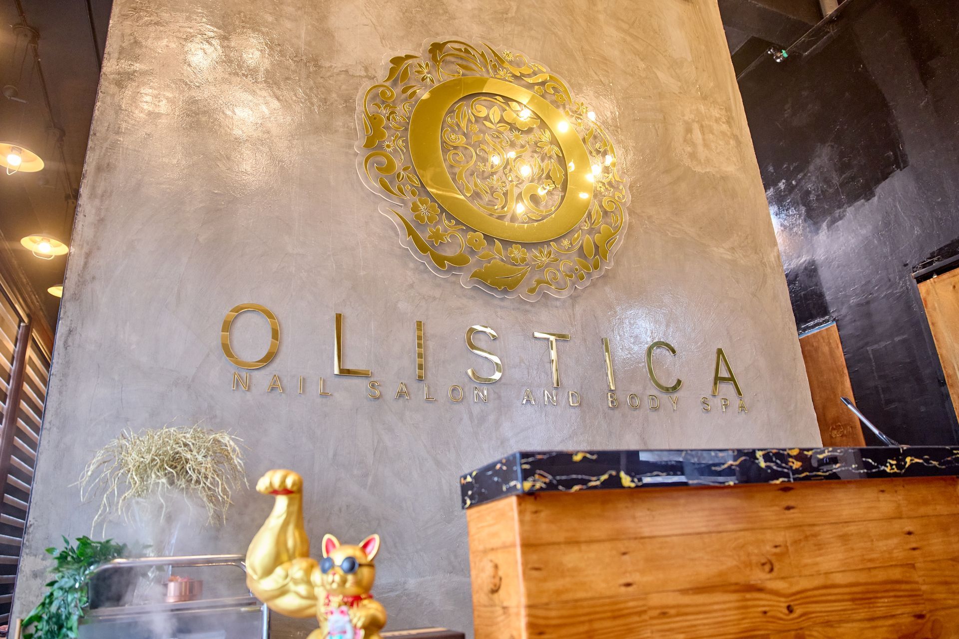 Entrance to Olistica Nail Salon and Body Spa, gold signage on textured wall, golden decorative art, reception desk, cat figurine.