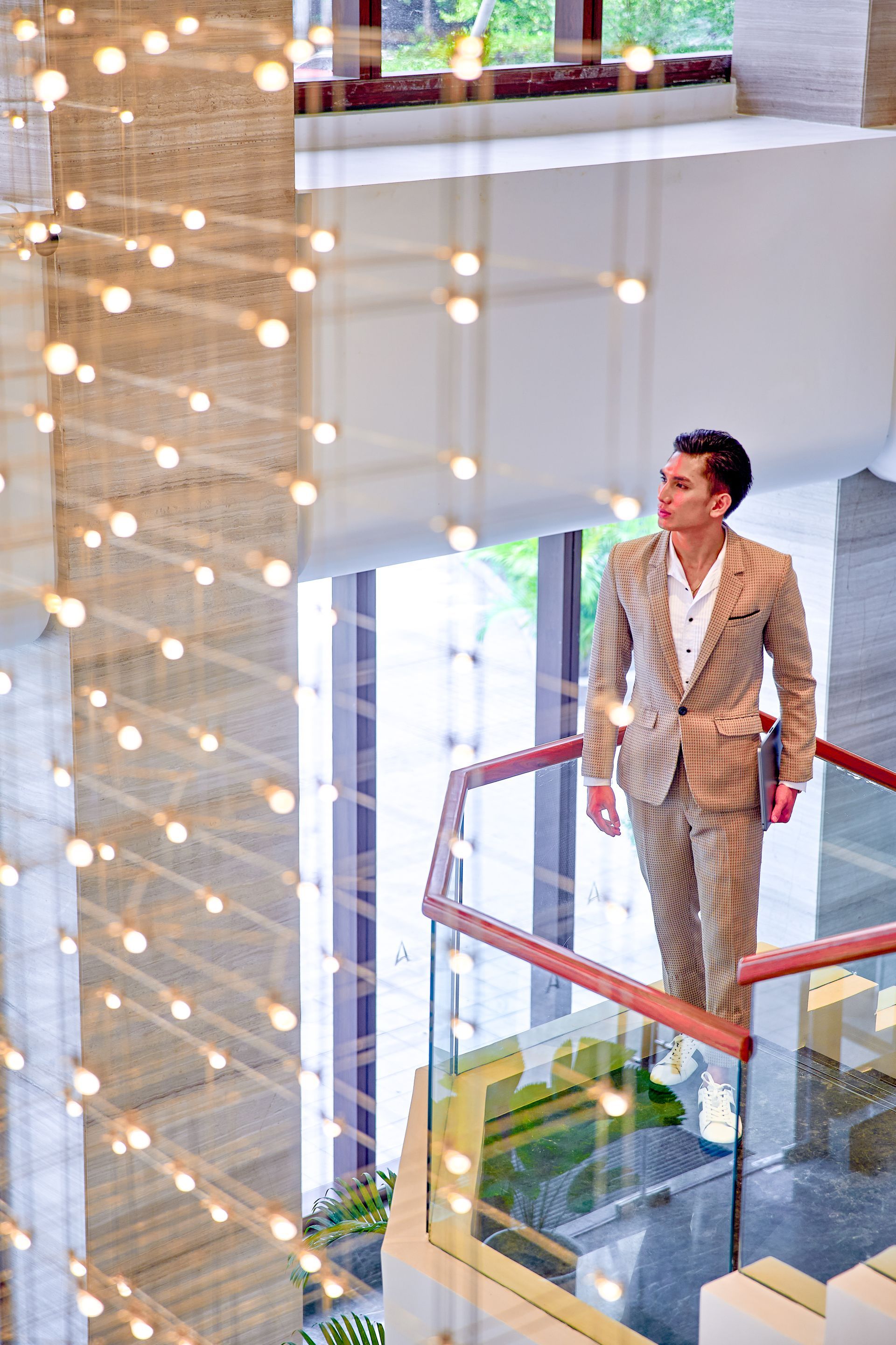 Man in suit, holding a laptop, on a staircase in a modern building, looking upwards.
