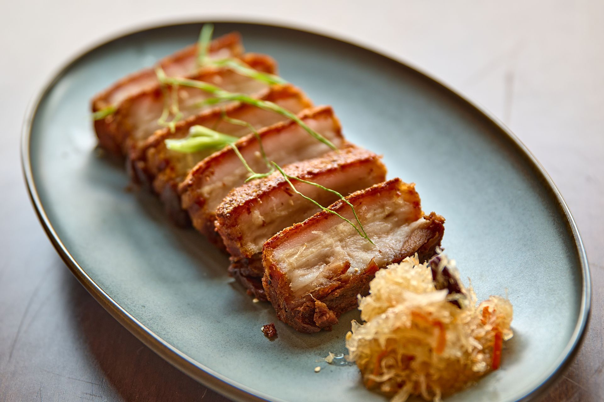 Sliced crispy pork belly with garnish on a blue oval plate.