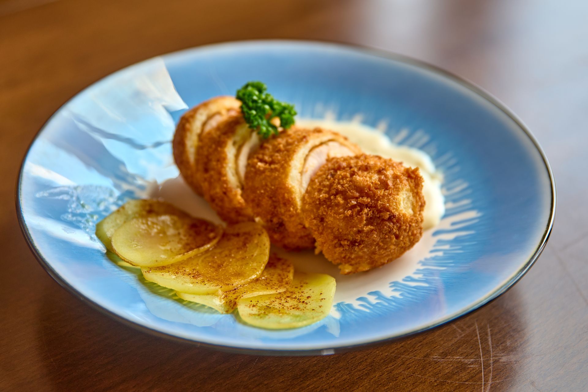 Sliced, breaded chicken breast on blue plate with potato slices and parsley garnish.