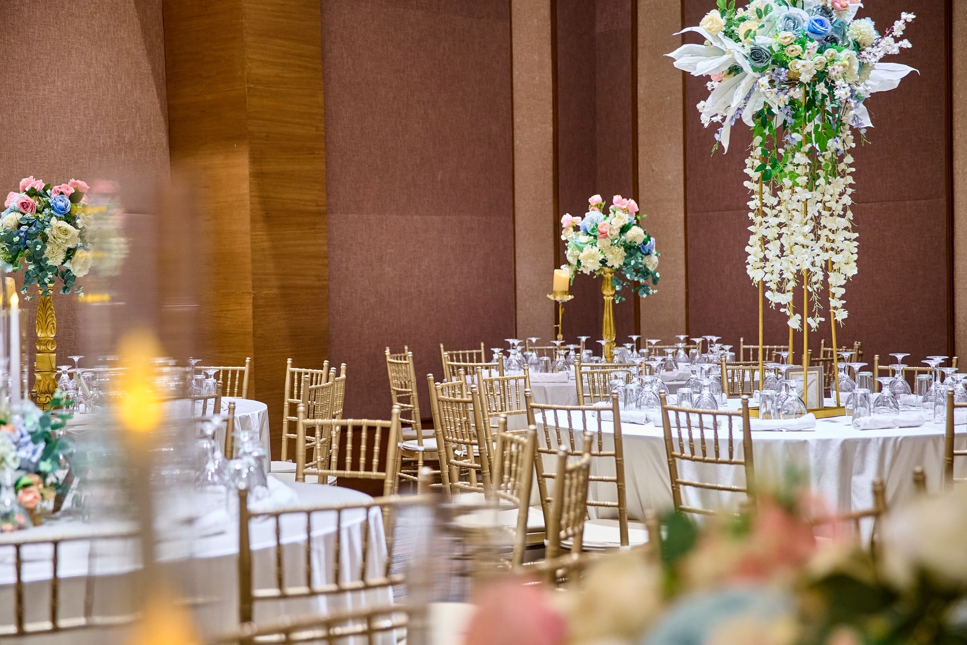 Elegant banquet hall with round tables, gold chairs, and floral centerpieces.
