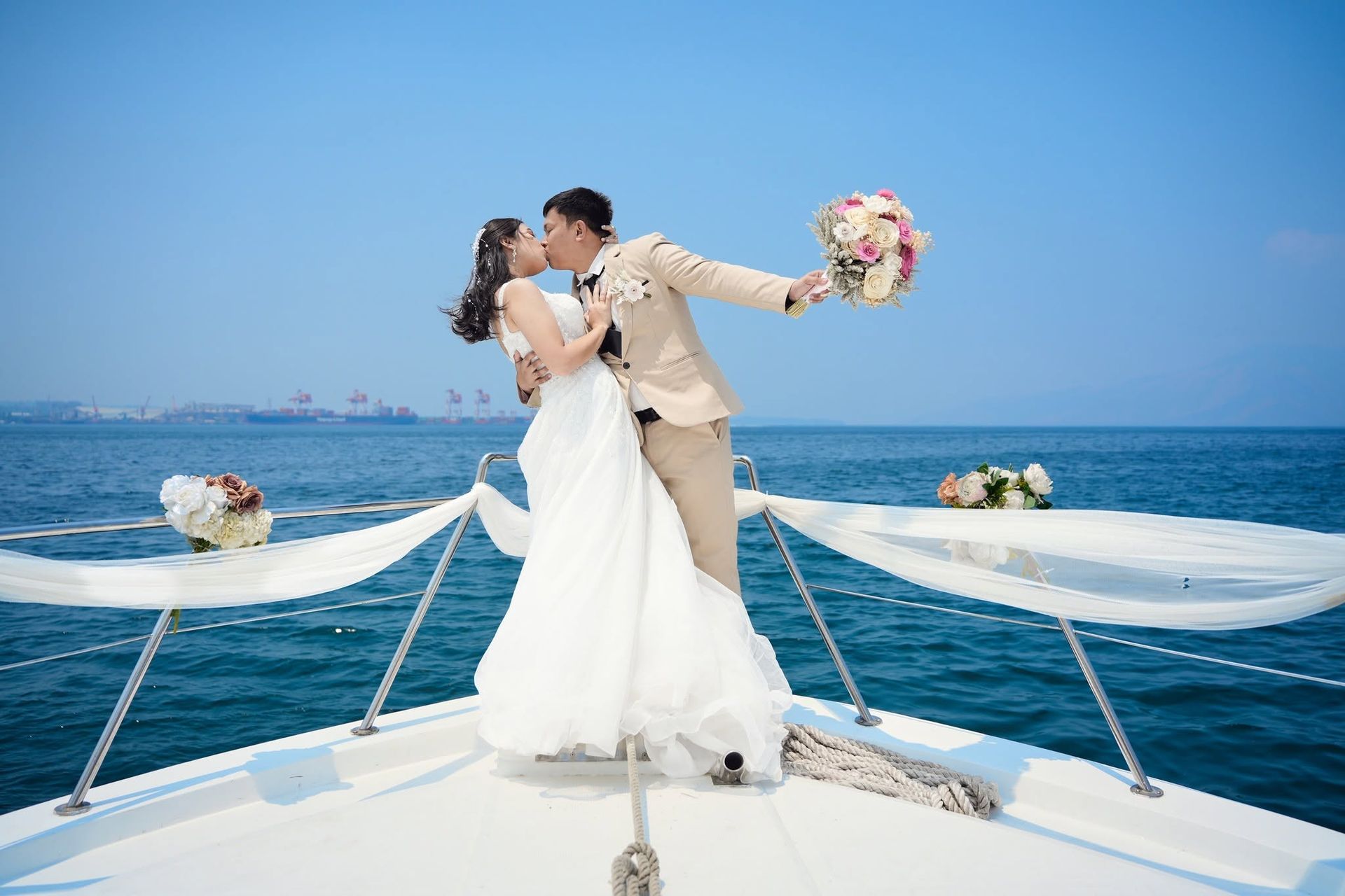 Bride and groom kiss on a yacht deck with ocean and blue sky behind them