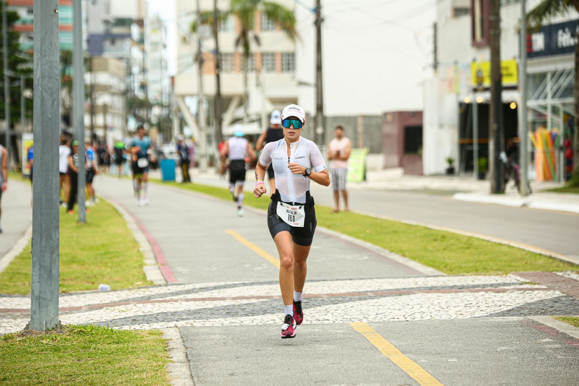 Triathlete running on a paved path during a race, wearing a white jersey and visor; urban setting.