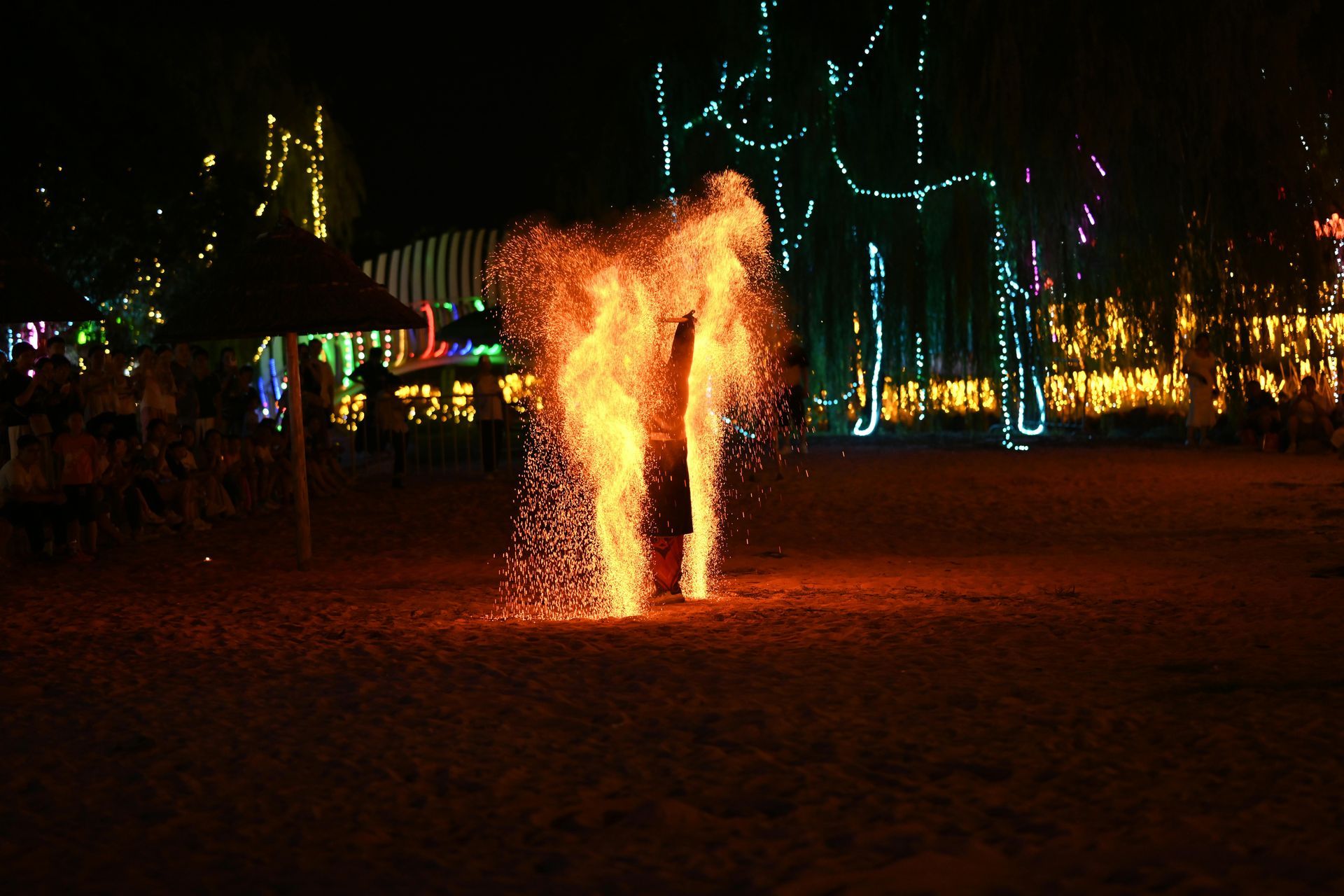 Fire performers create a spark display on a beach at night.