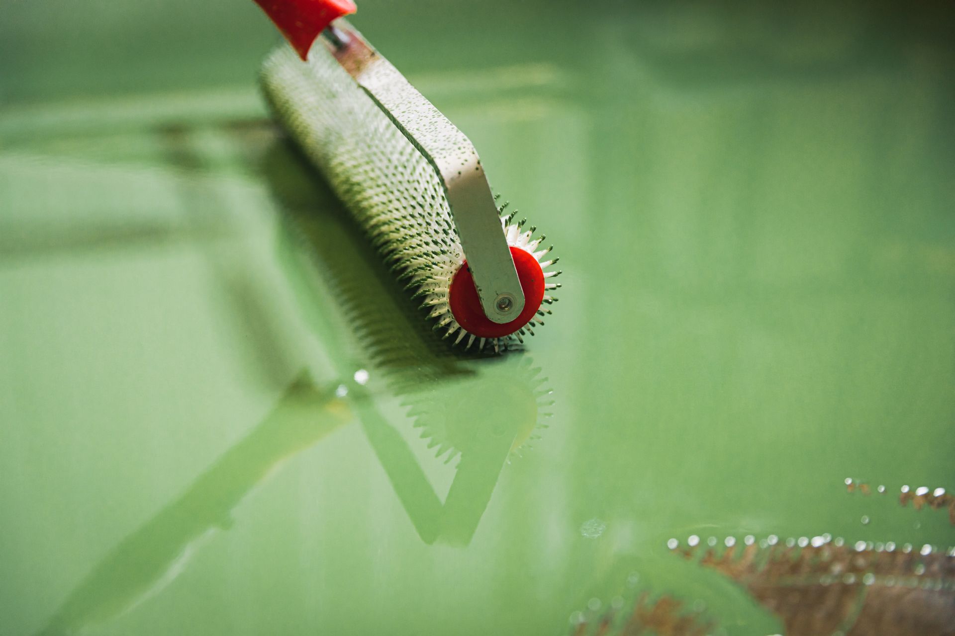 A roller is being used to paint a green floor.