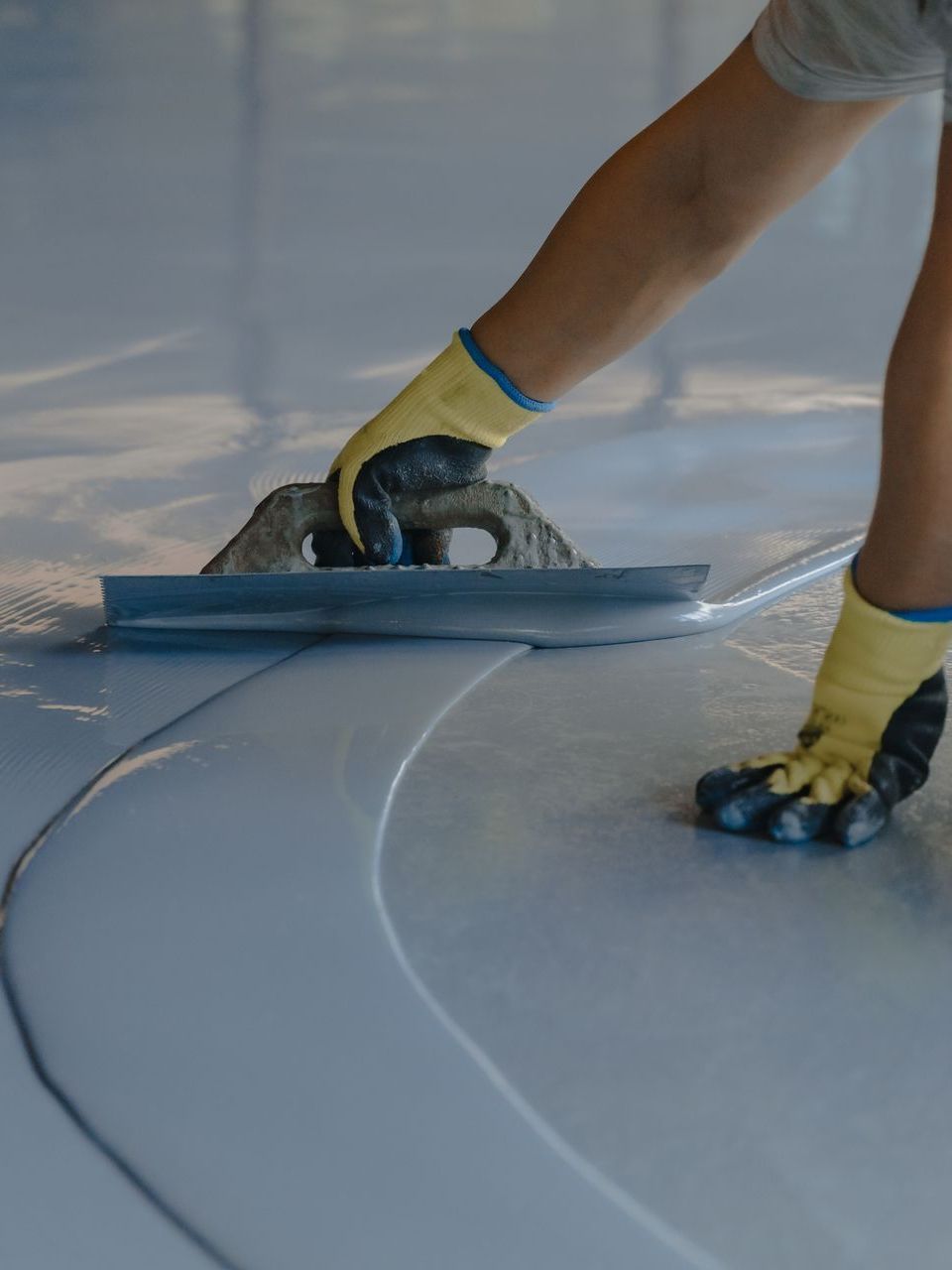 A person wearing yellow gloves is using a trowel on a white floor.