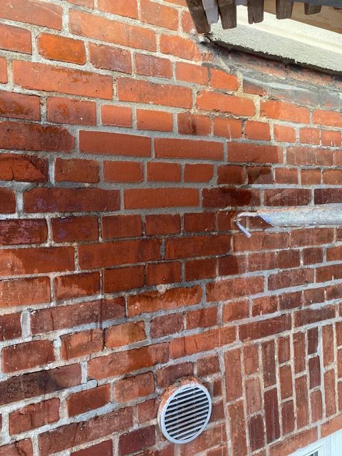 Ydervæg af rød mursten med udluftning og tagrende.