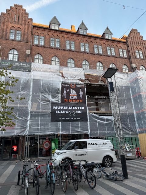 Bygning under renovering med stillads og en hvid varevogn parkeret foran.