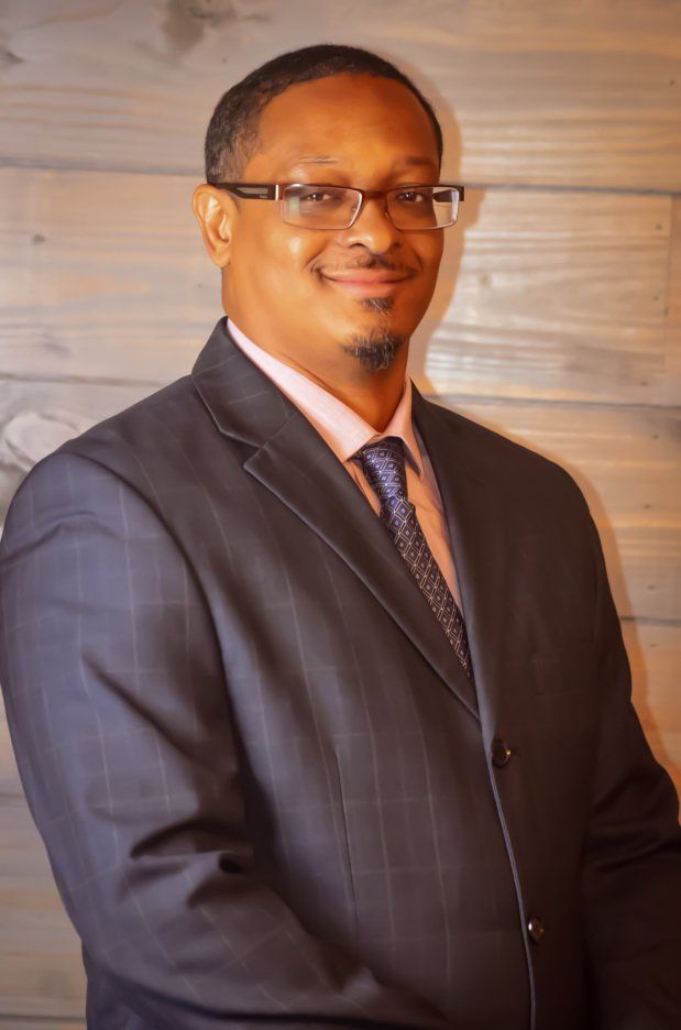 A man in a suit and tie is standing in front of a wooden wall.