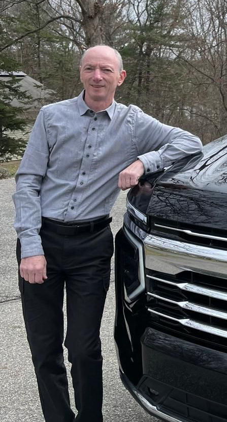 A man in a suit and tie is standing in front of a car