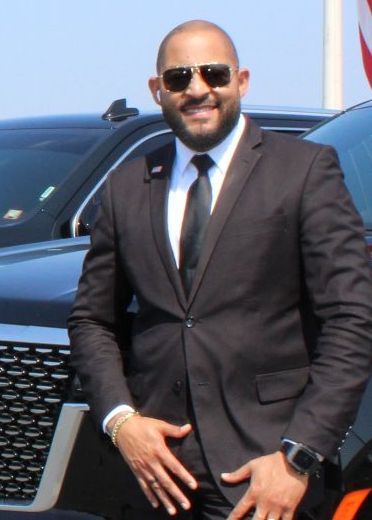 A man in a suit and tie is standing in front of a car