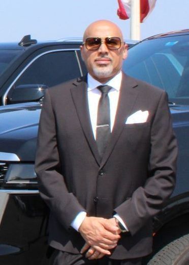 A man in a suit and tie is standing in front of a car