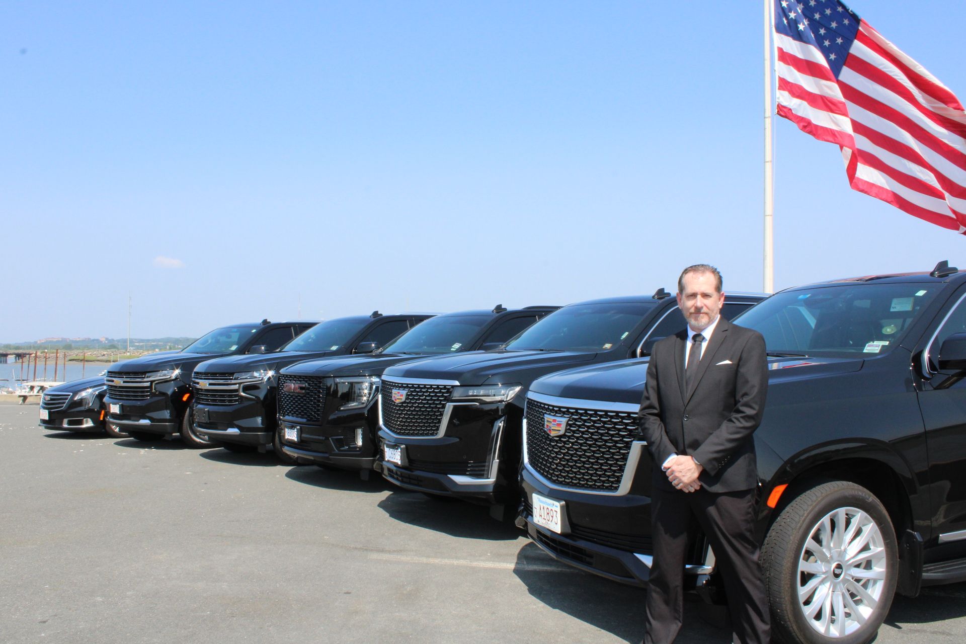 A man in a suit and tie is standing in front of a row of cars.