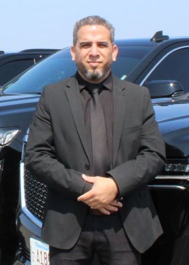 A man in a suit and tie is standing in front of two cars