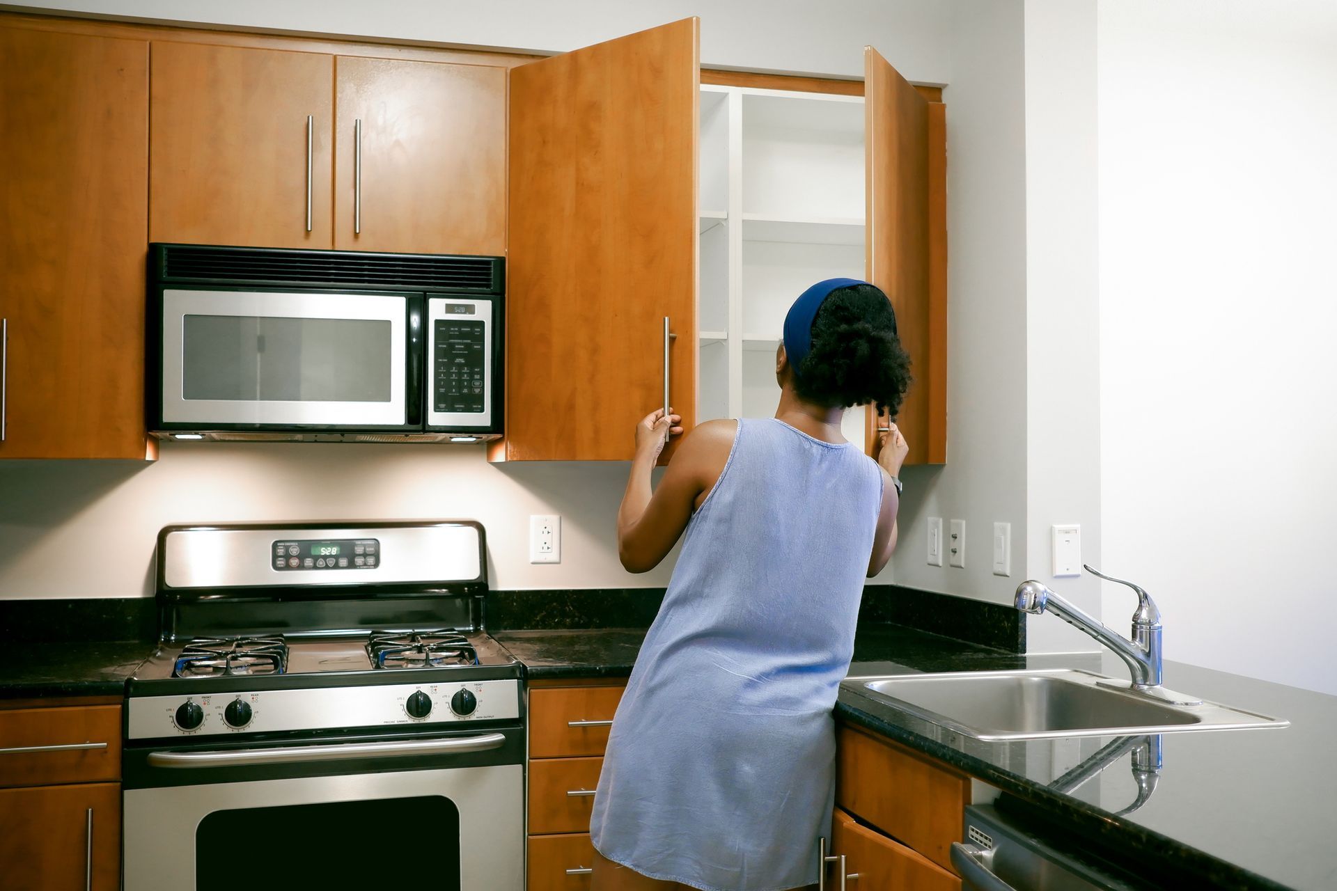 A woman opens a cabinet door in a kitchen, highlighting stylish new cabinets and a functional space.