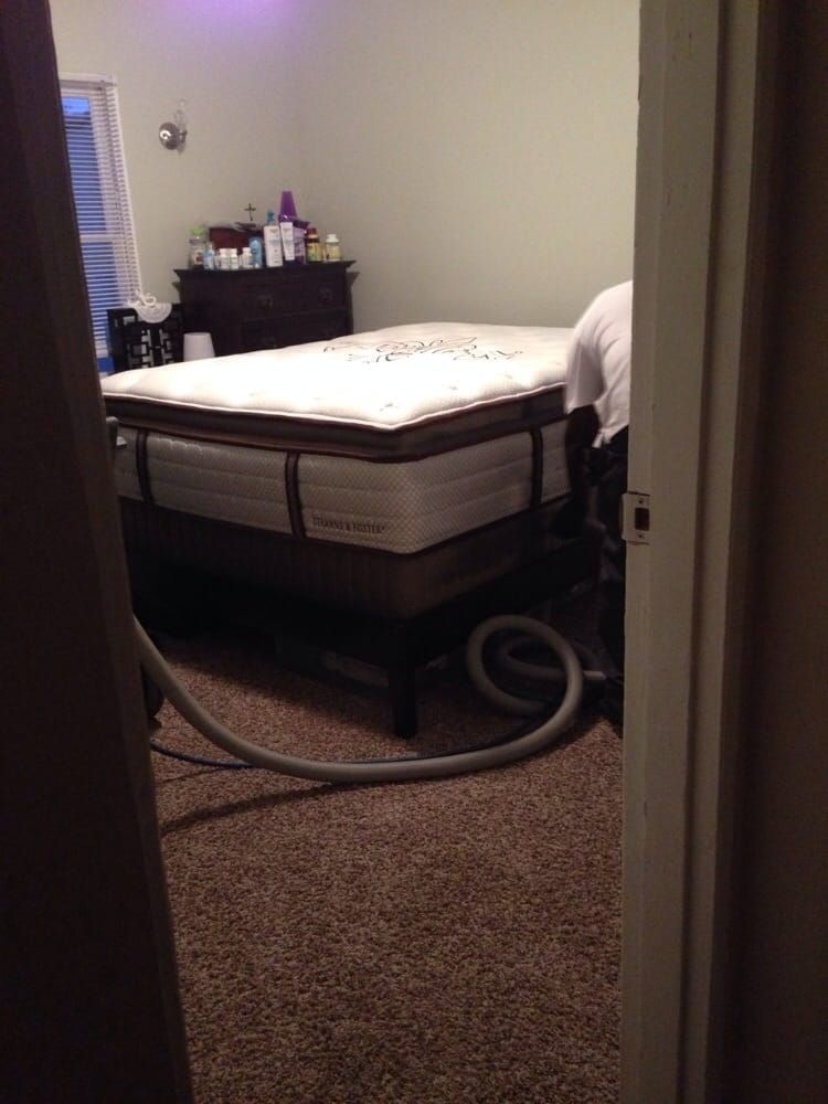 A bed is sitting in a bedroom with a vacuum hose attached to it.