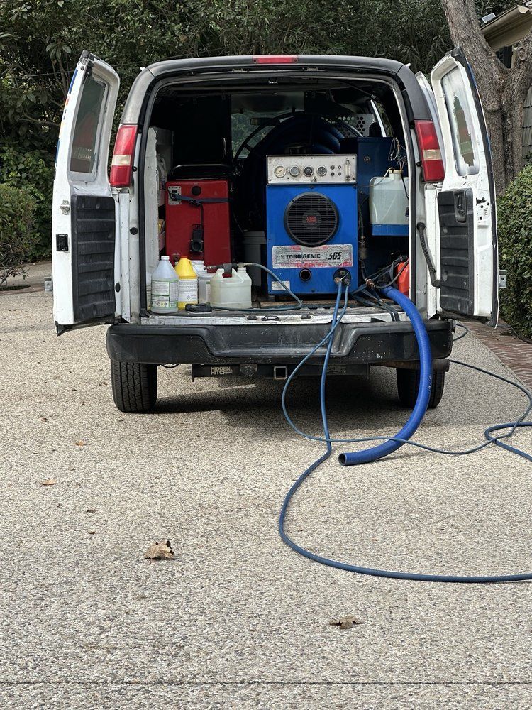 A white van with a vacuum cleaner in the back is parked in a driveway.