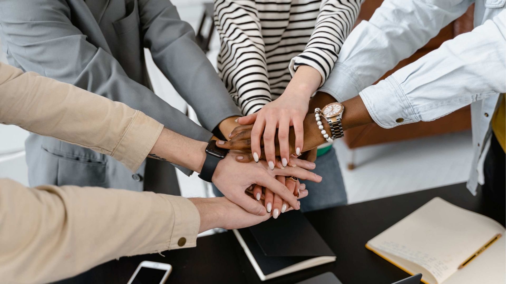 Hands stacked together in a group huddle, symbolizing teamwork and unity.