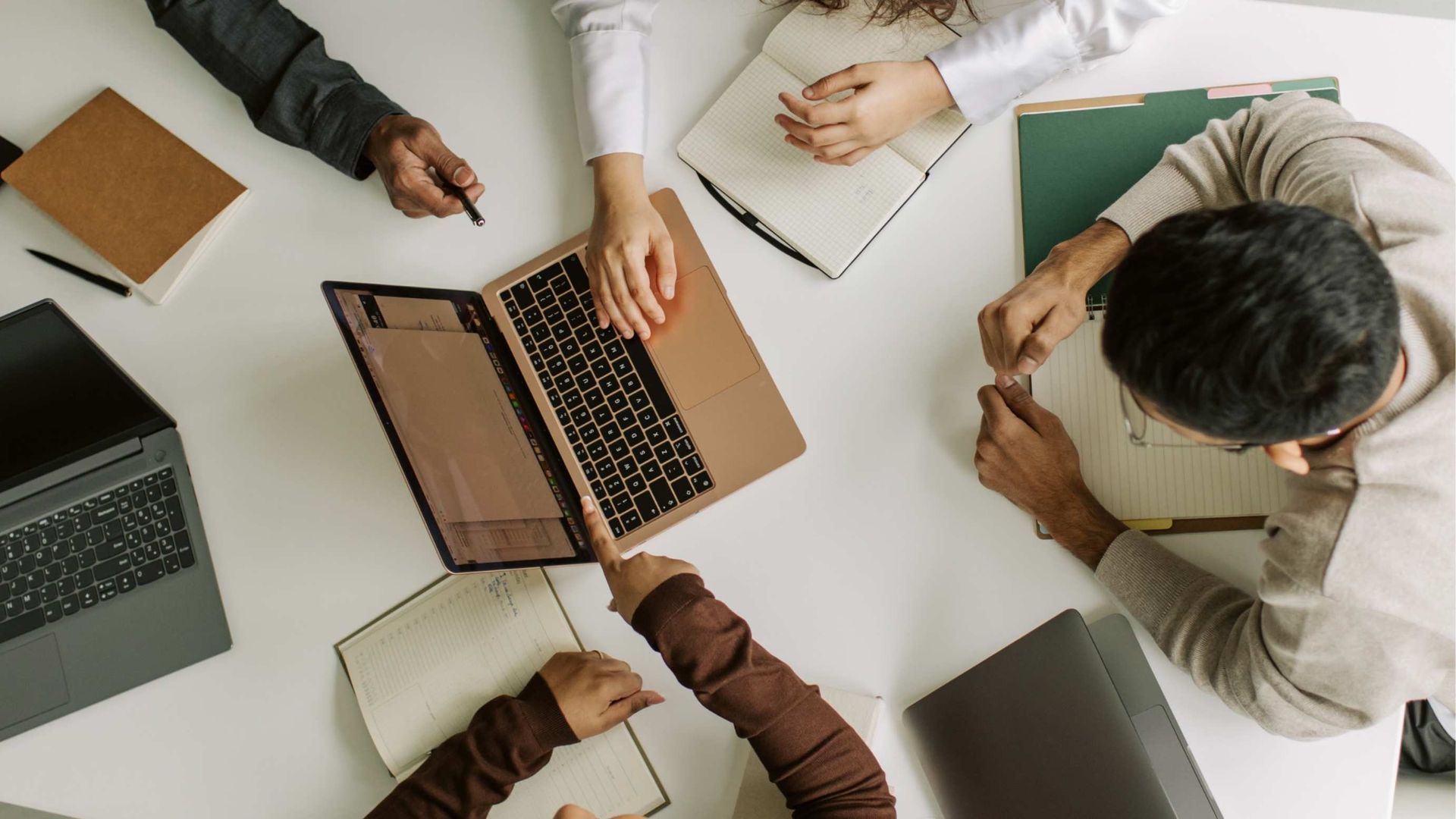 People around a table, working on laptops and notebooks; collaborative meeting.