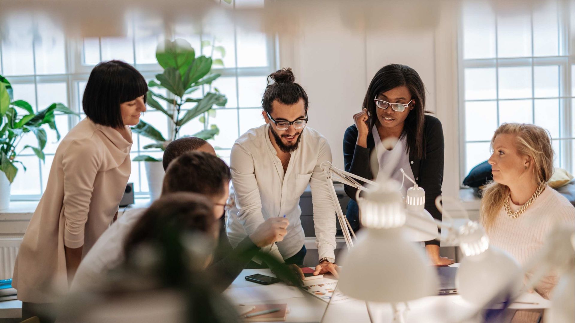 Group of diverse colleagues gathered around a table in a bright office, collaborating on a project.