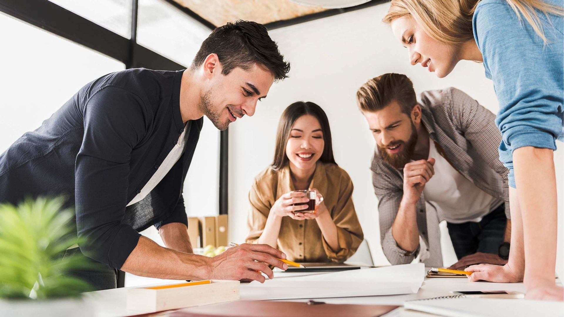 A diverse team collaborates around a table, reviewing blueprints, smiling in a modern office.